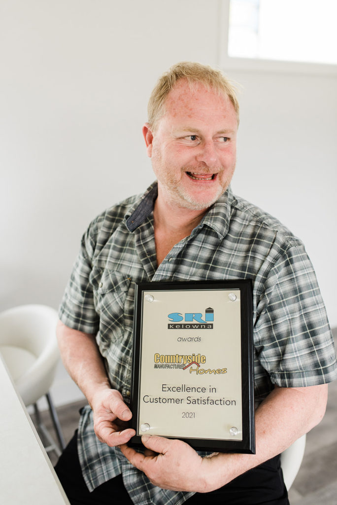 frank ambler jr, co-owner of countryside manufactured homes, holds a plaque commemorating business building excellence in Kamloops and Shuswap