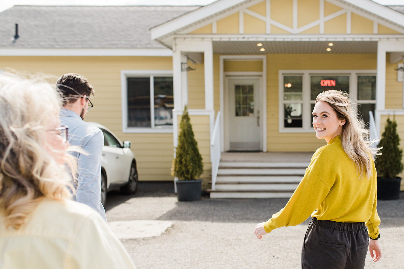 young blonde woman wearing a mustard yellow sweater looks back and smiles as she walks into the office at countryside manufactured homes in Kamloops