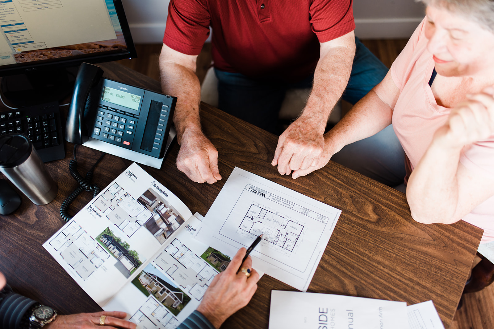 a retired couple hold hands while looking over their modular home plans with a sales rep at countryside manufactured homes